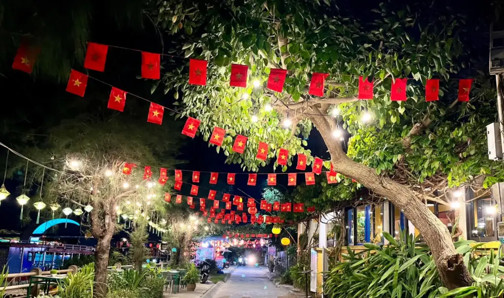 Huyen Tran Cong Chua riverside street in Hoi An at night with flags and string lights